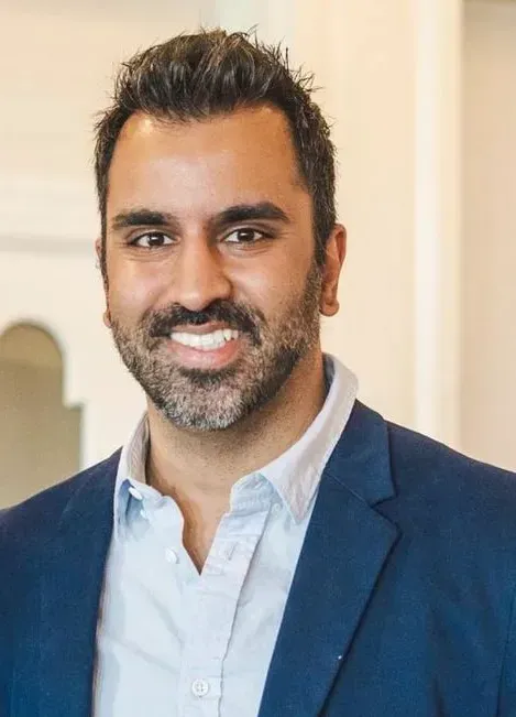 Portrait of a smiling man in a blue blazer and white shirt against a light indoor background