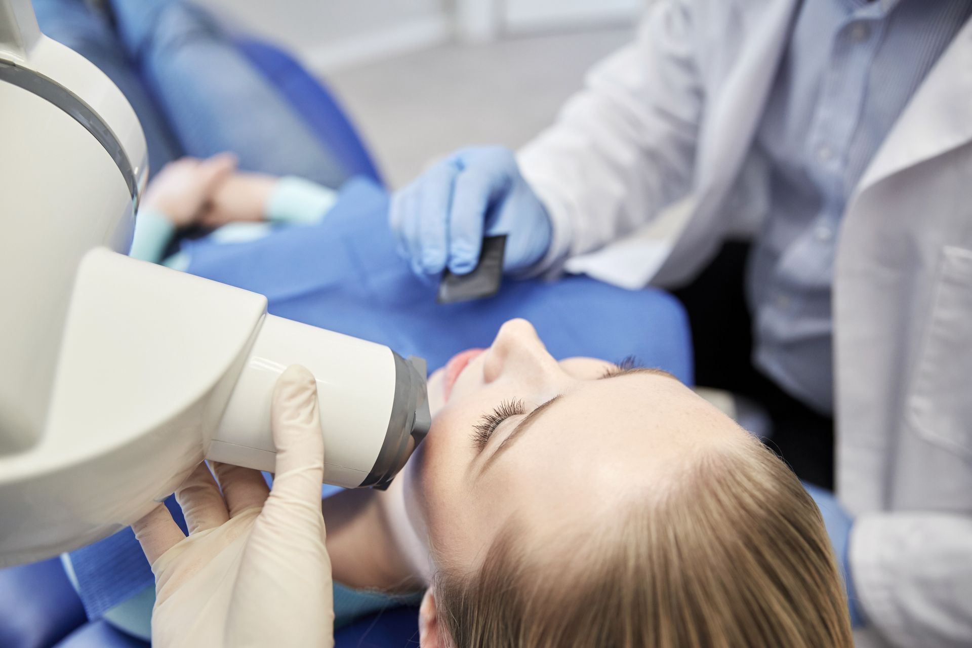 Dental exam with a patient reclined in a chair while a dentist uses imaging equipment near her face