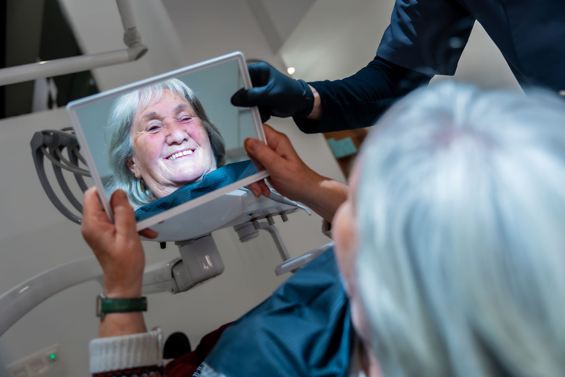 Nurse holding a tablet showing a smiling patient during a telehealth exam in a clinic
