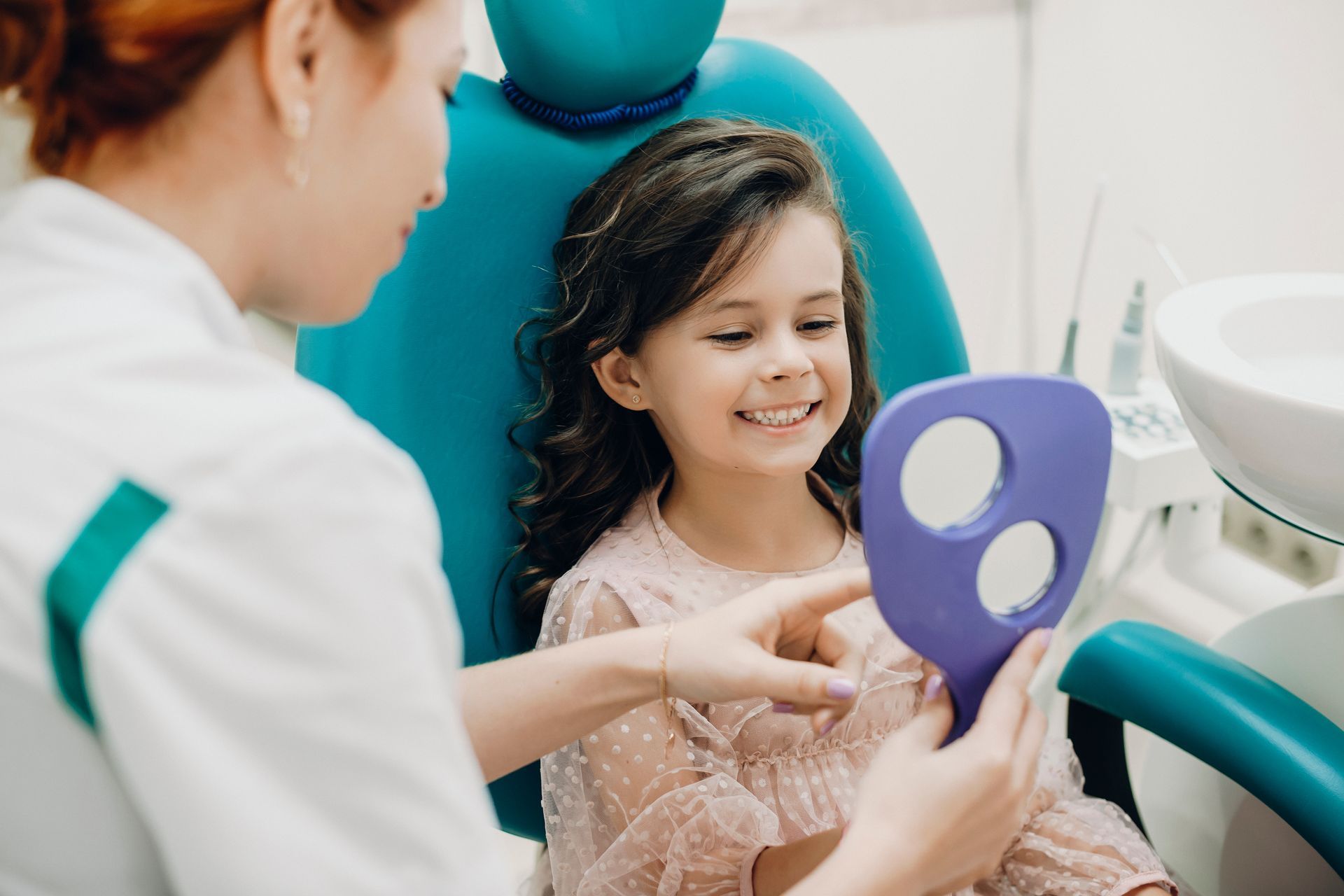 Child smiling at a dentist while holding a purple dental mirror in a clinic