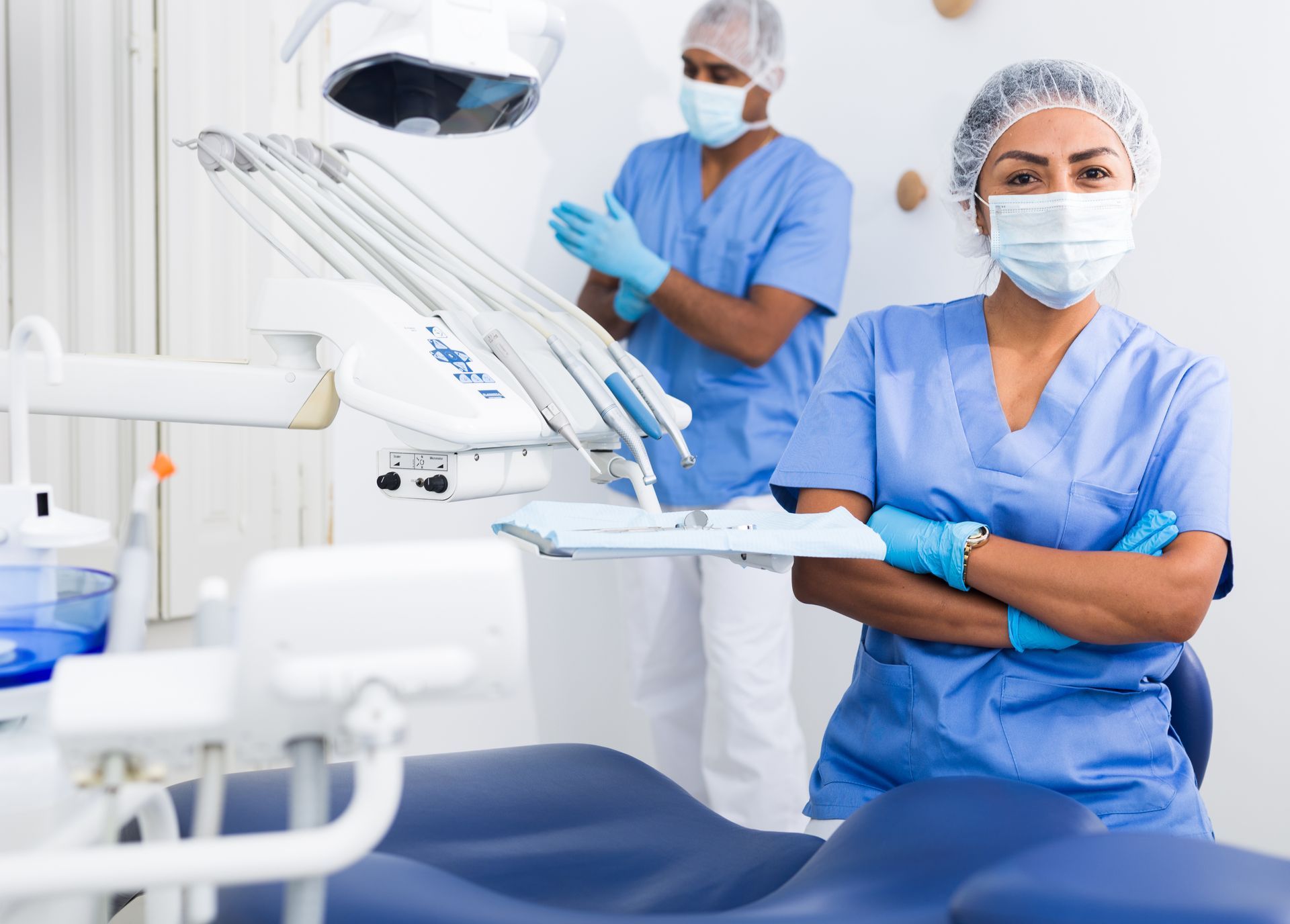 Dentist and assistant in blue scrubs and masks in a modern dental clinic, with a dental chair and equipment nearby