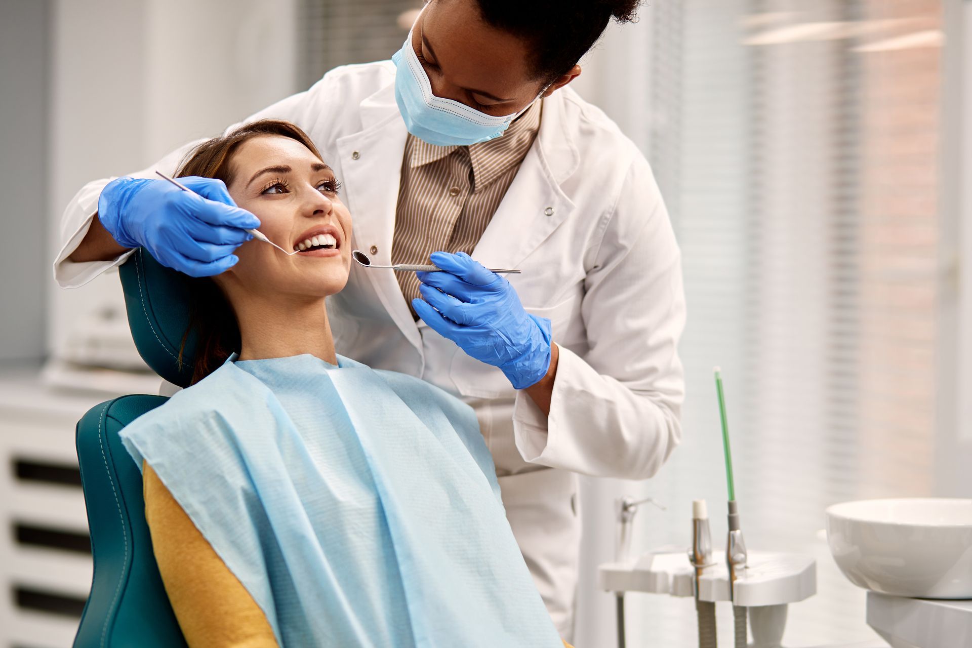 Dentist wearing gloves and mask examining a seated patient in a dental clinic