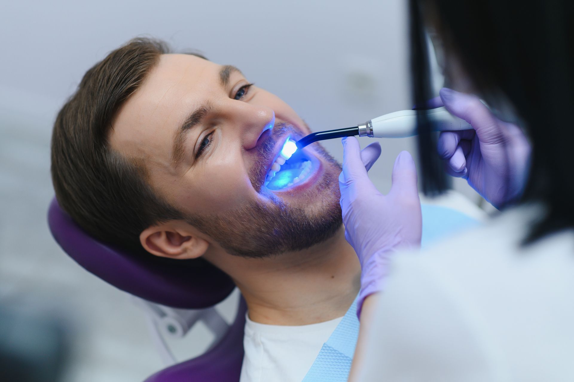 Dentist using a blue curing light on a patient’s teeth in a dental chair