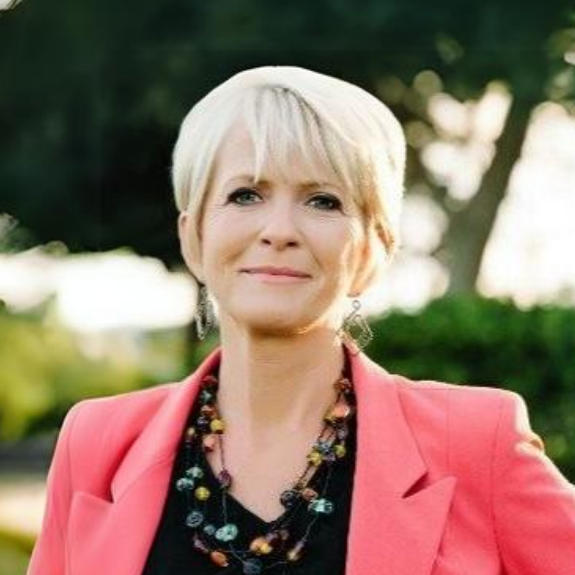 The woman is wearing a pink jacket and a necklace.