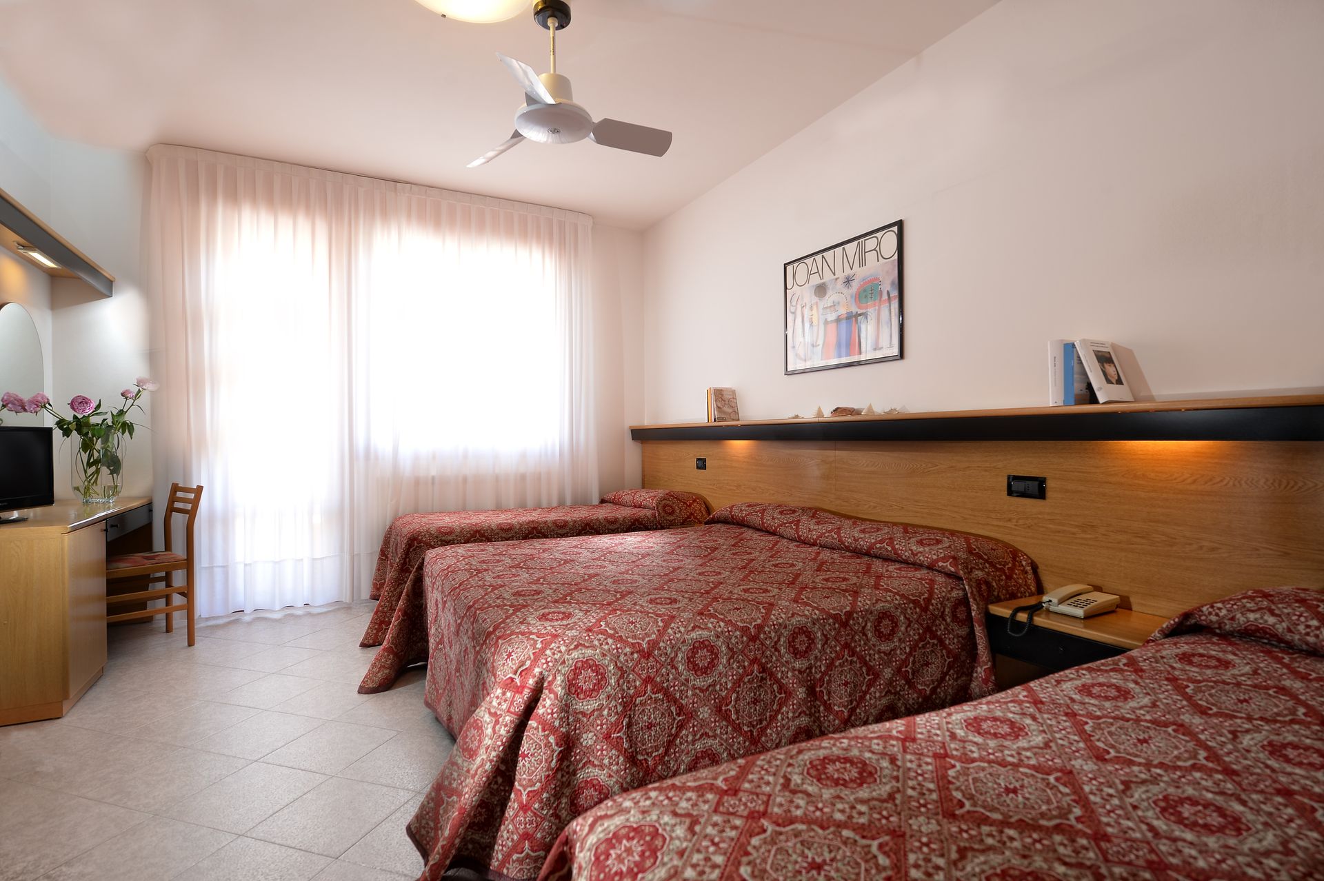 A hotel room with three beds and a ceiling fan
