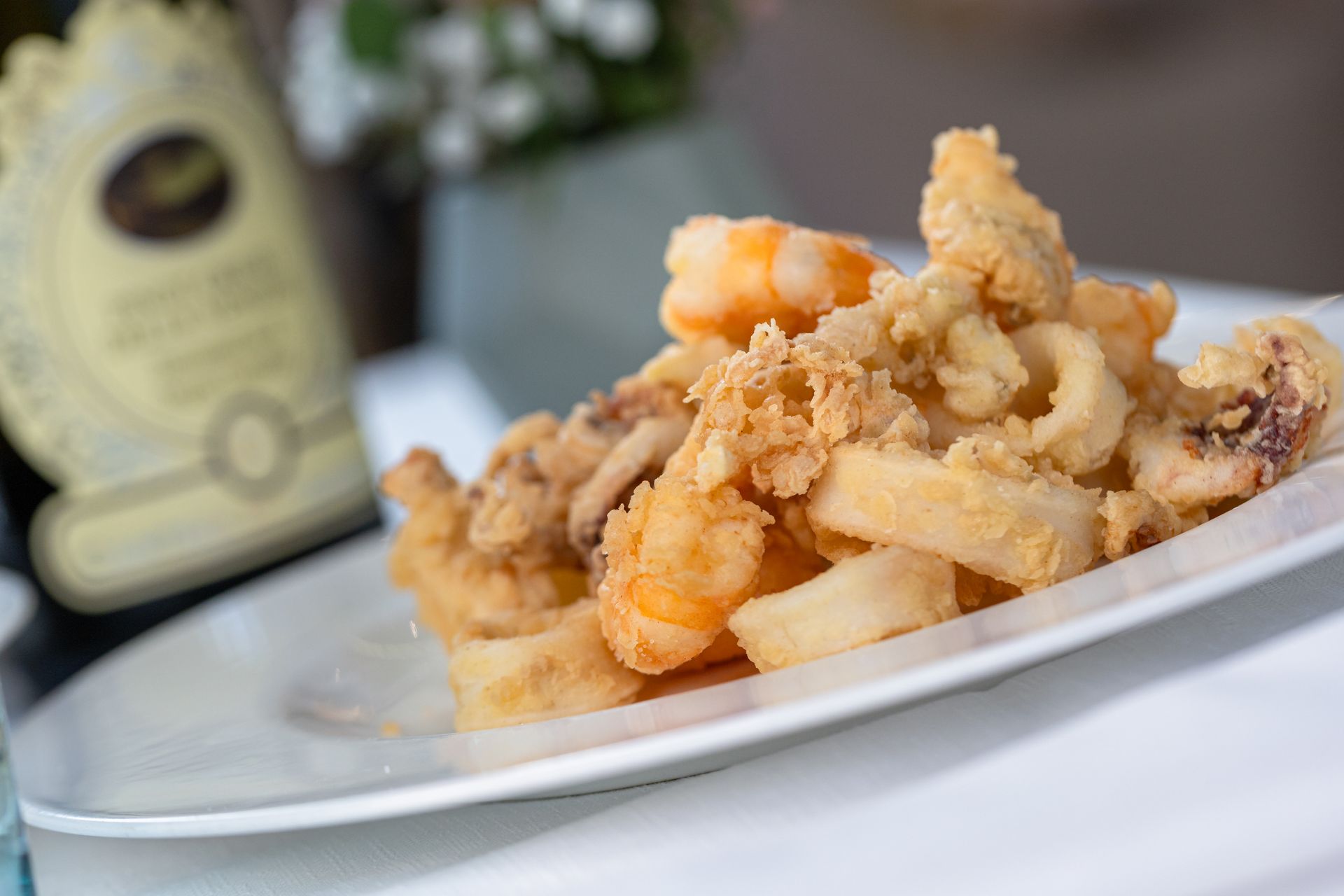 A plate of fried seafood with a bottle of wine in the background.