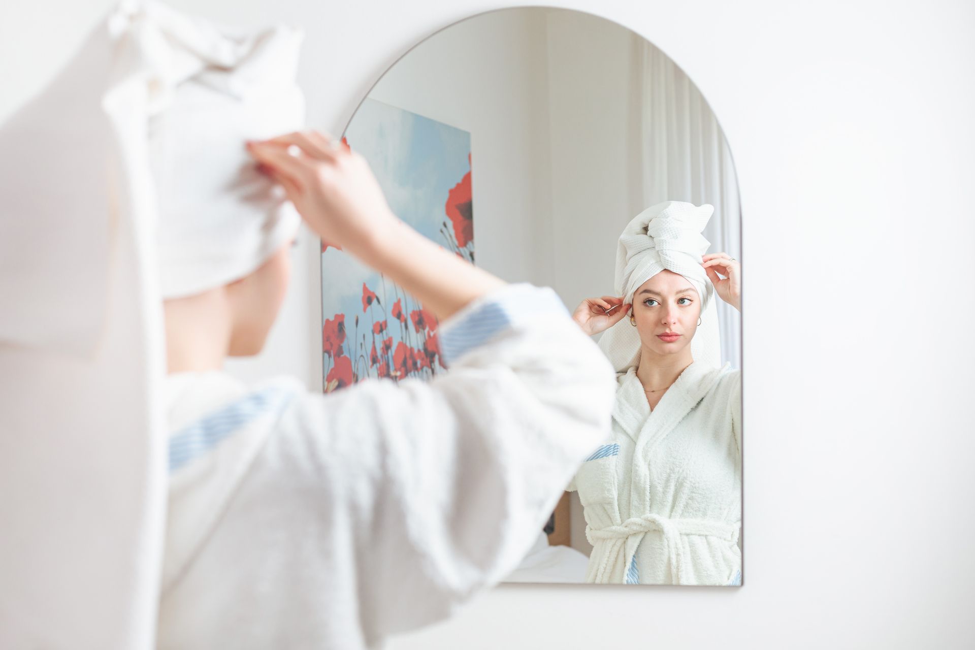 A woman in a bathrobe is looking at her reflection in a mirror.