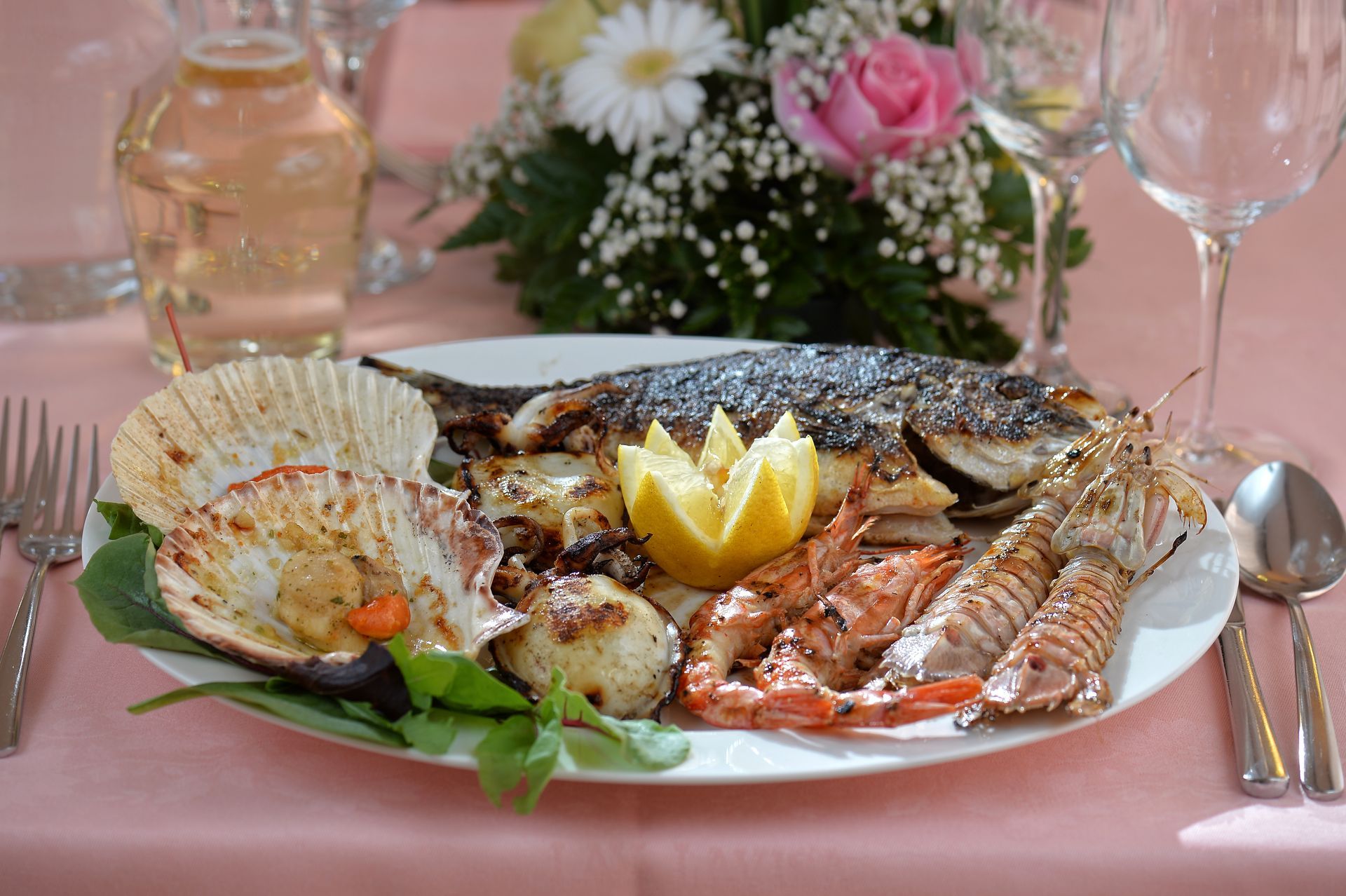 Un piatto di pesce e frutti di mare su un tavolo con un mazzo di fiori sullo sfondo.