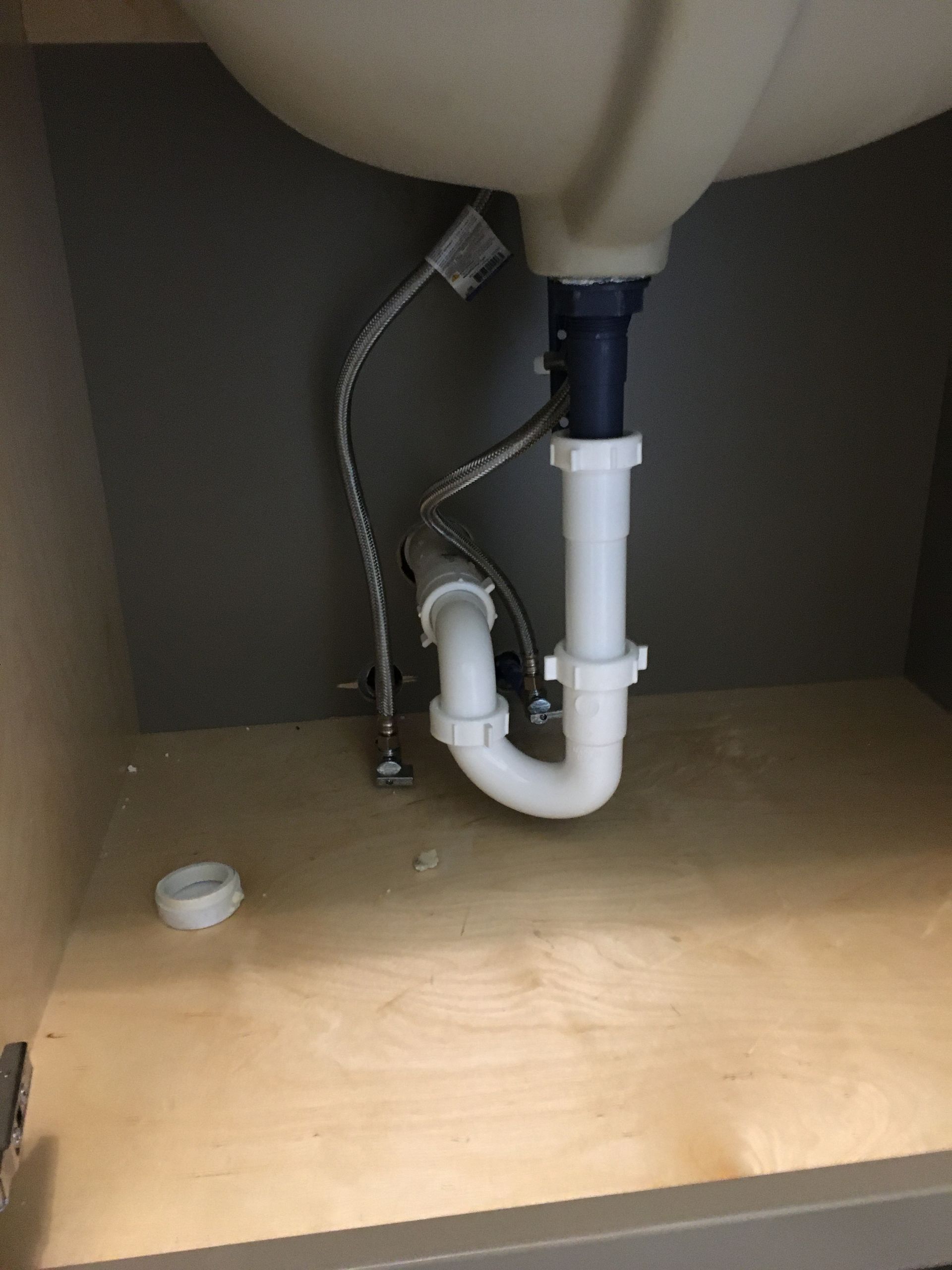 Under-sink plumbing with white PVC pipes and hoses beneath a sink cabinet.