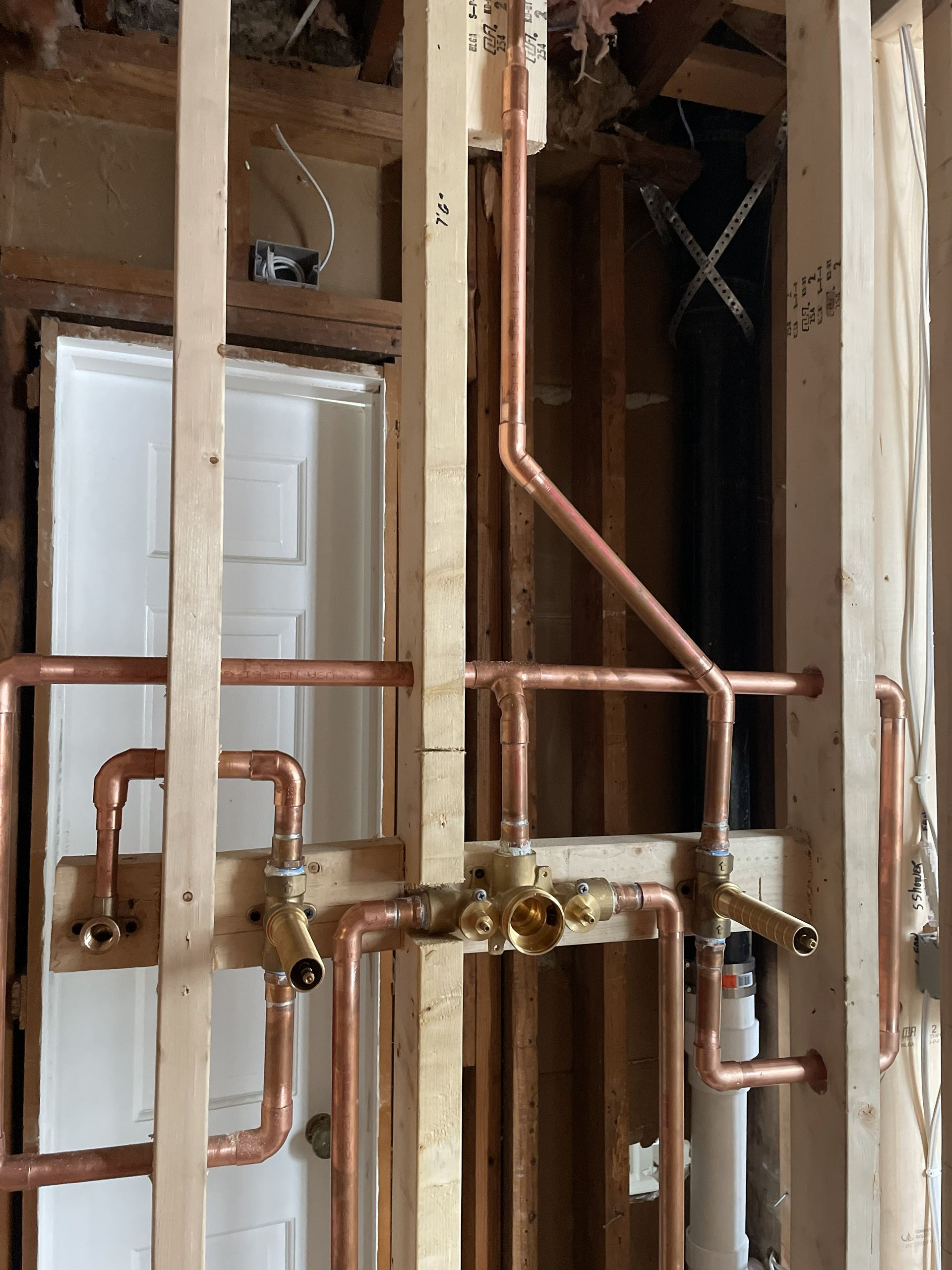 Partially finished wall with exposed copper pipes, framing, and a white door in the background