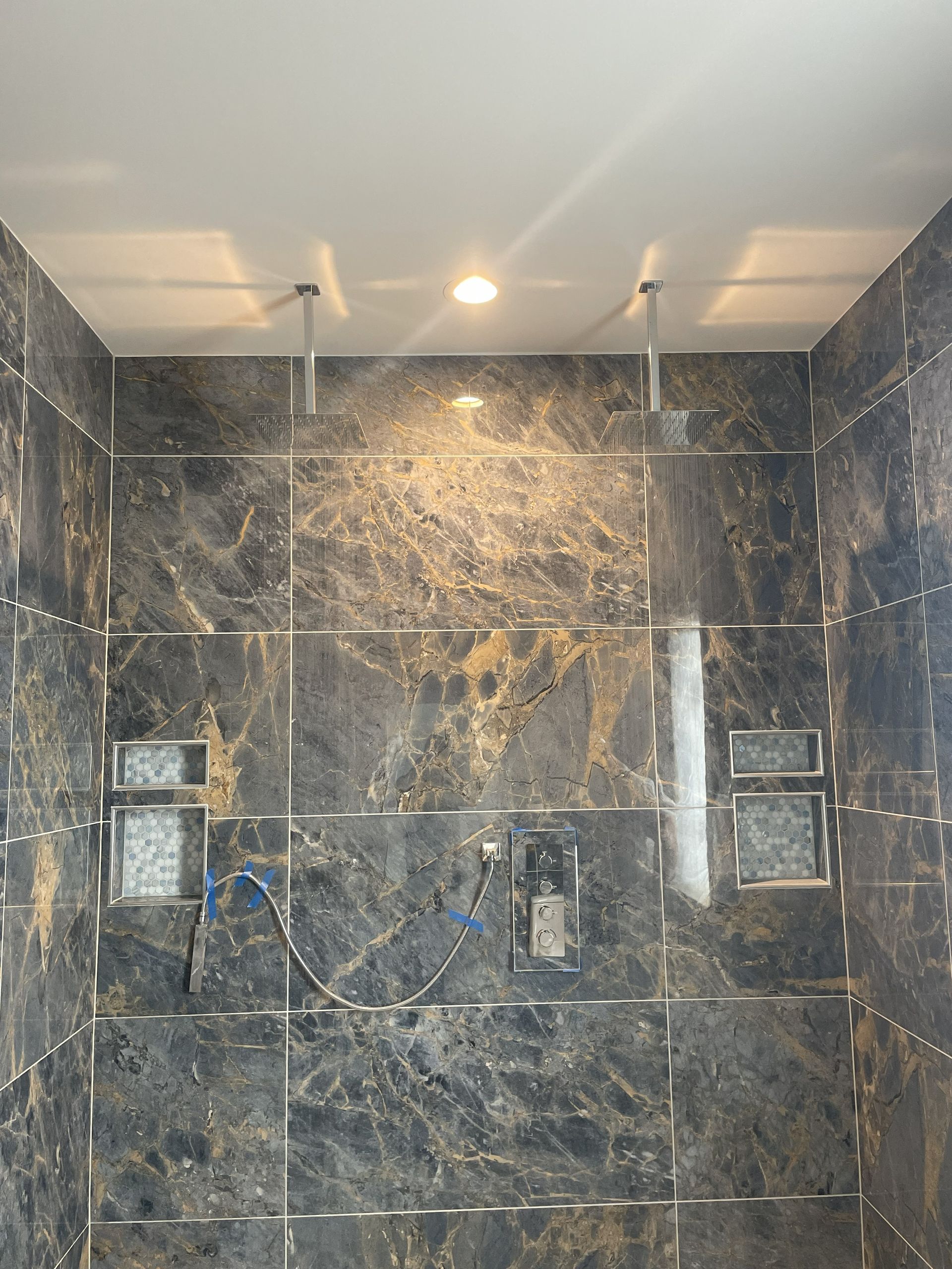 Dark marble-tiled shower with built-in niches and a ceiling light above the center.