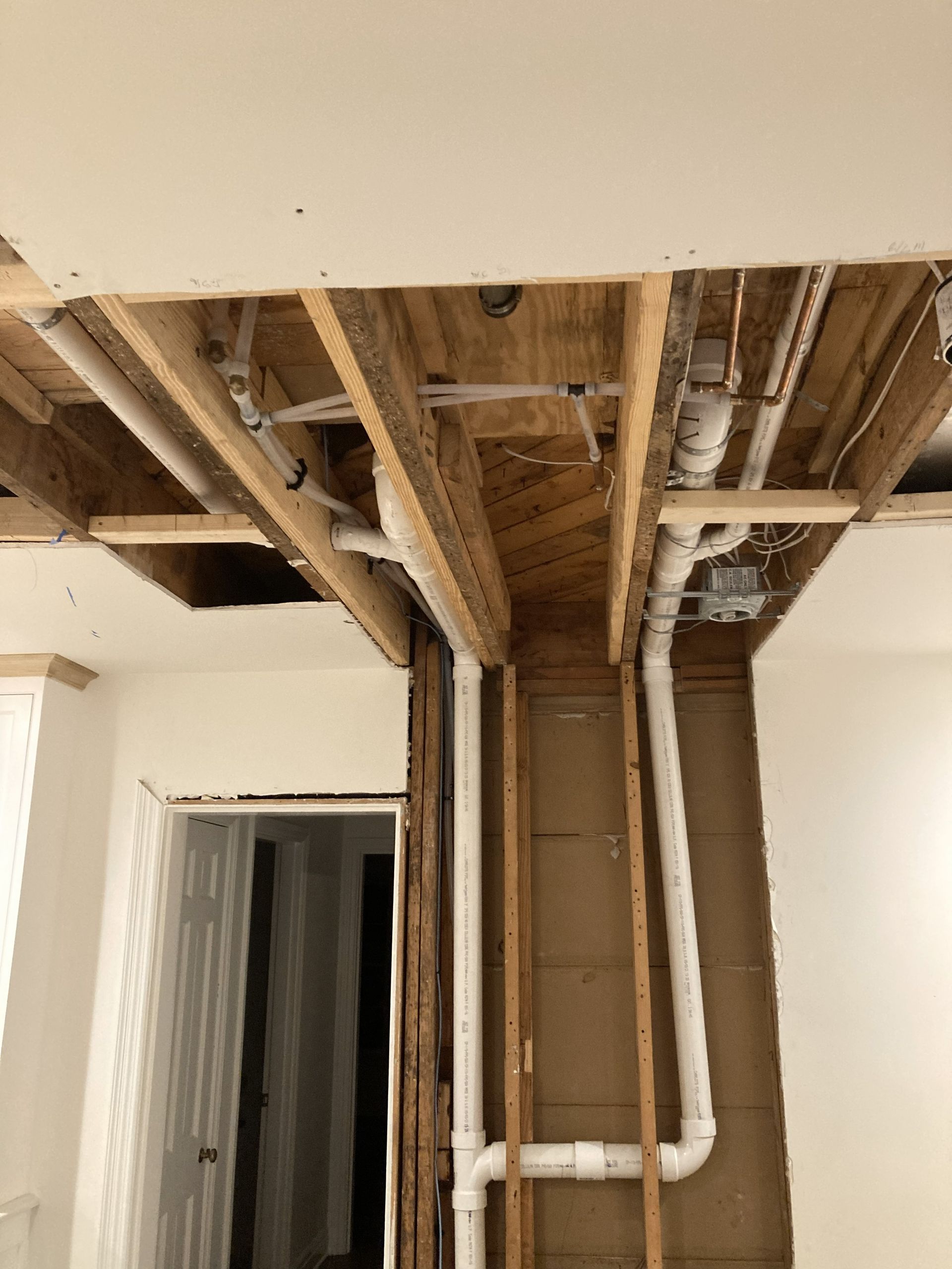 Exposed ceiling joists and pipes in a room under renovation, with a doorway below.