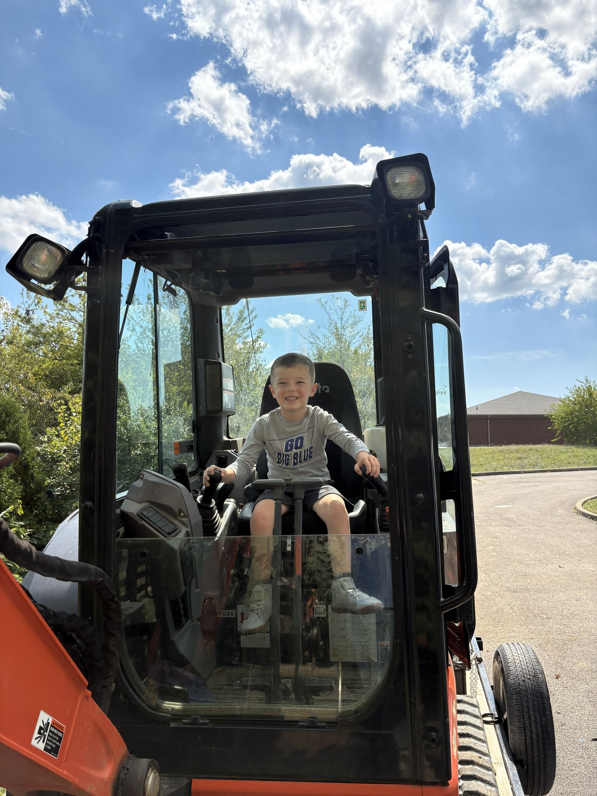 Child sitting in a black tractor cab outdoors under a blue sky