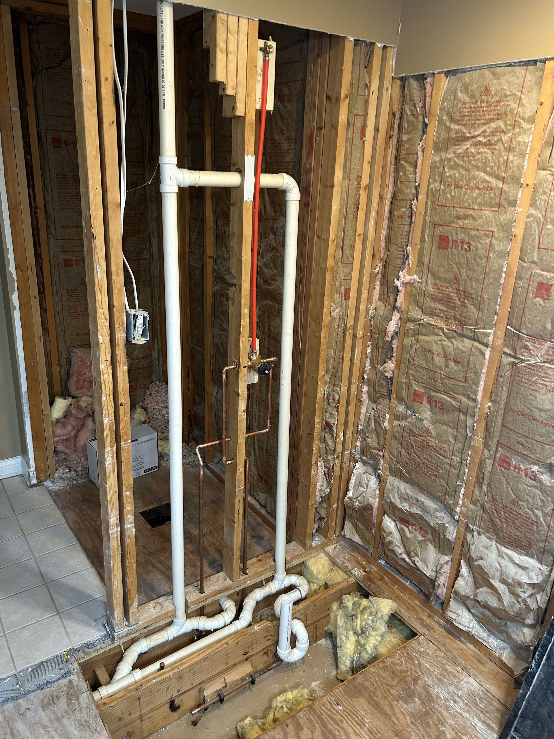 Unfinished bathroom wall with exposed framing, insulation, and white plumbing pipes during renovation