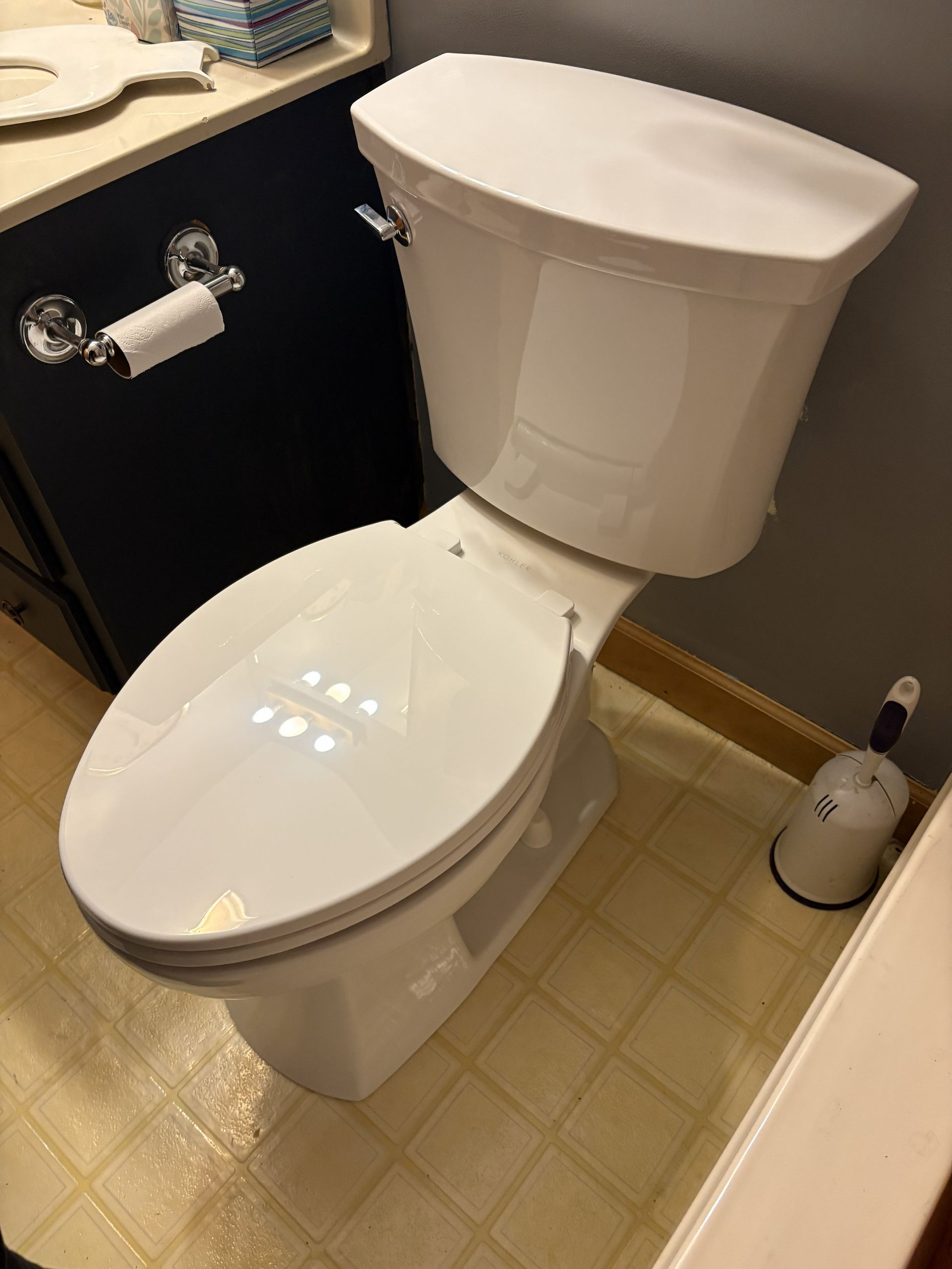 Small bathroom with a white toilet, beige floor tiles, and a toilet paper holder on the wall.