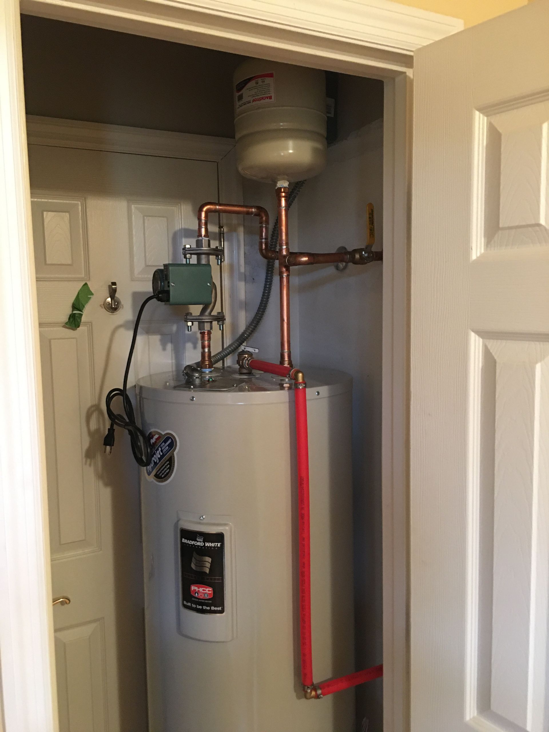 Water heater and plumbing in a closet with open doors.