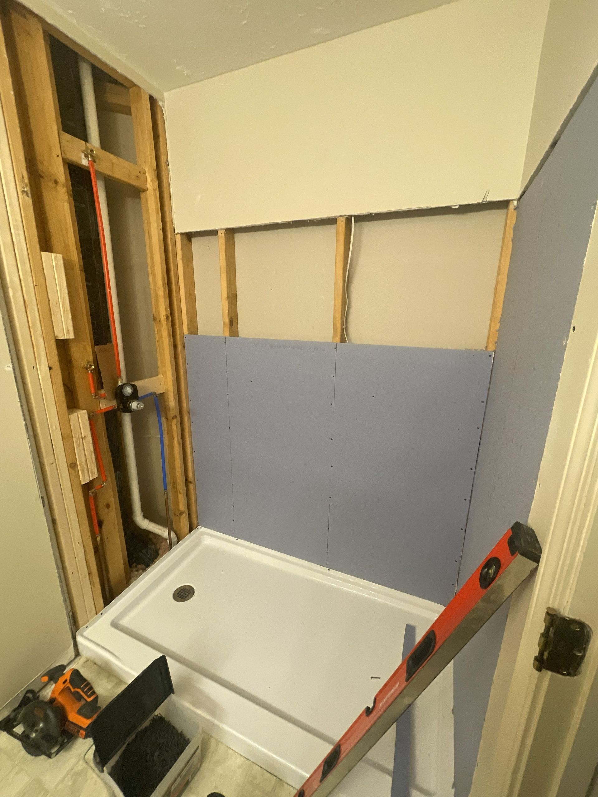 Bathroom under renovation with a shower base, exposed studs, and a red level on the wall