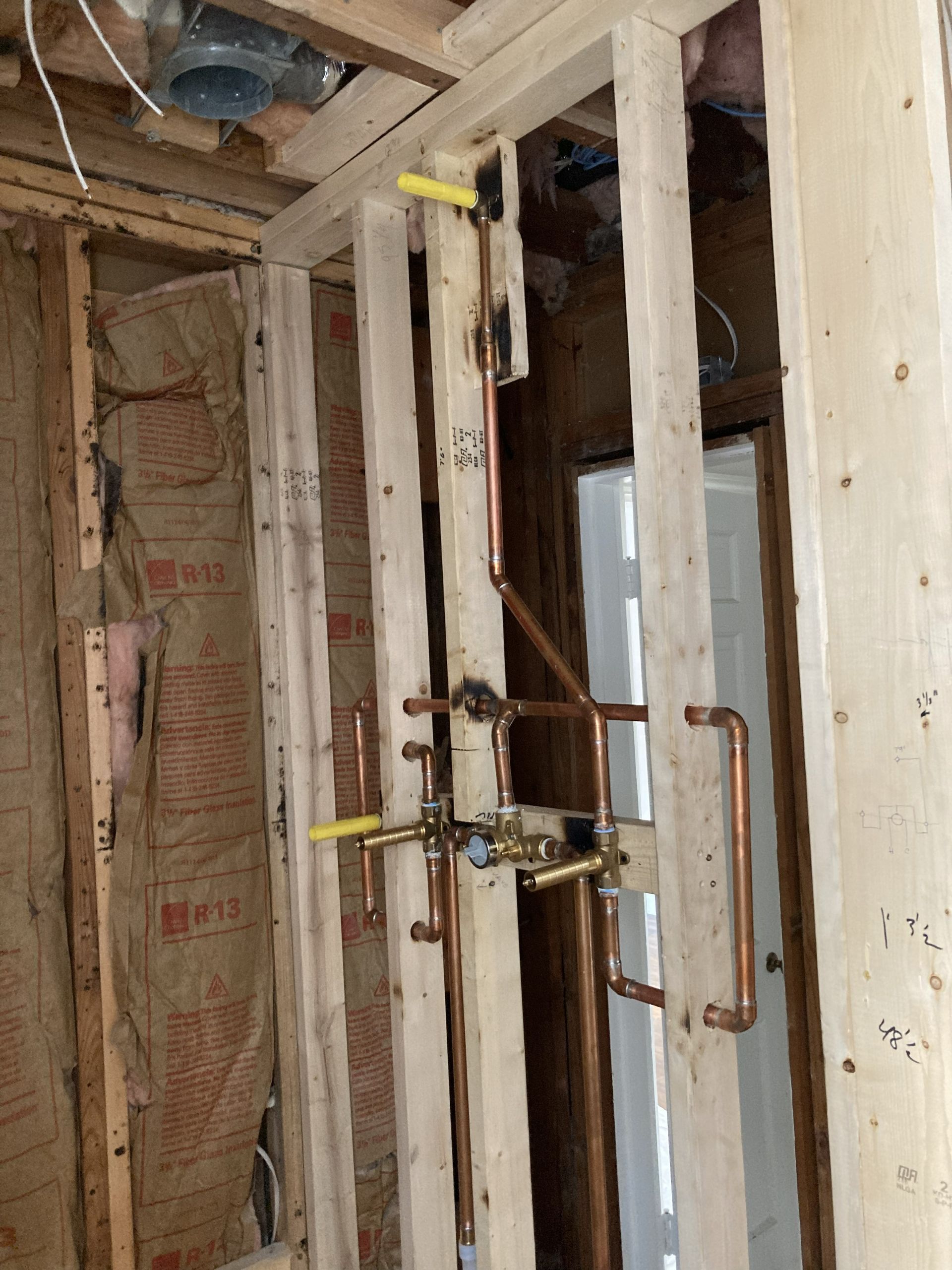 Partially finished wall framing with exposed insulation, plumbing pipes, and a copper tube in a renovation area