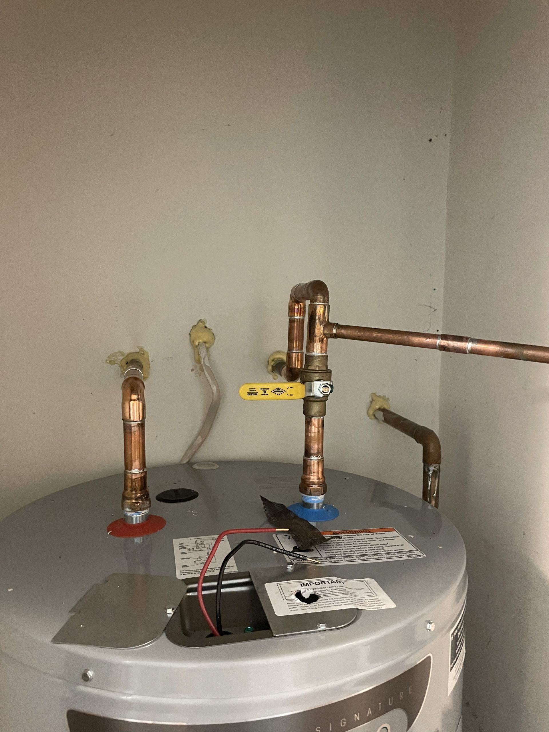 Top of a water heater with copper pipes and a yellow shutoff valve in a utility closet