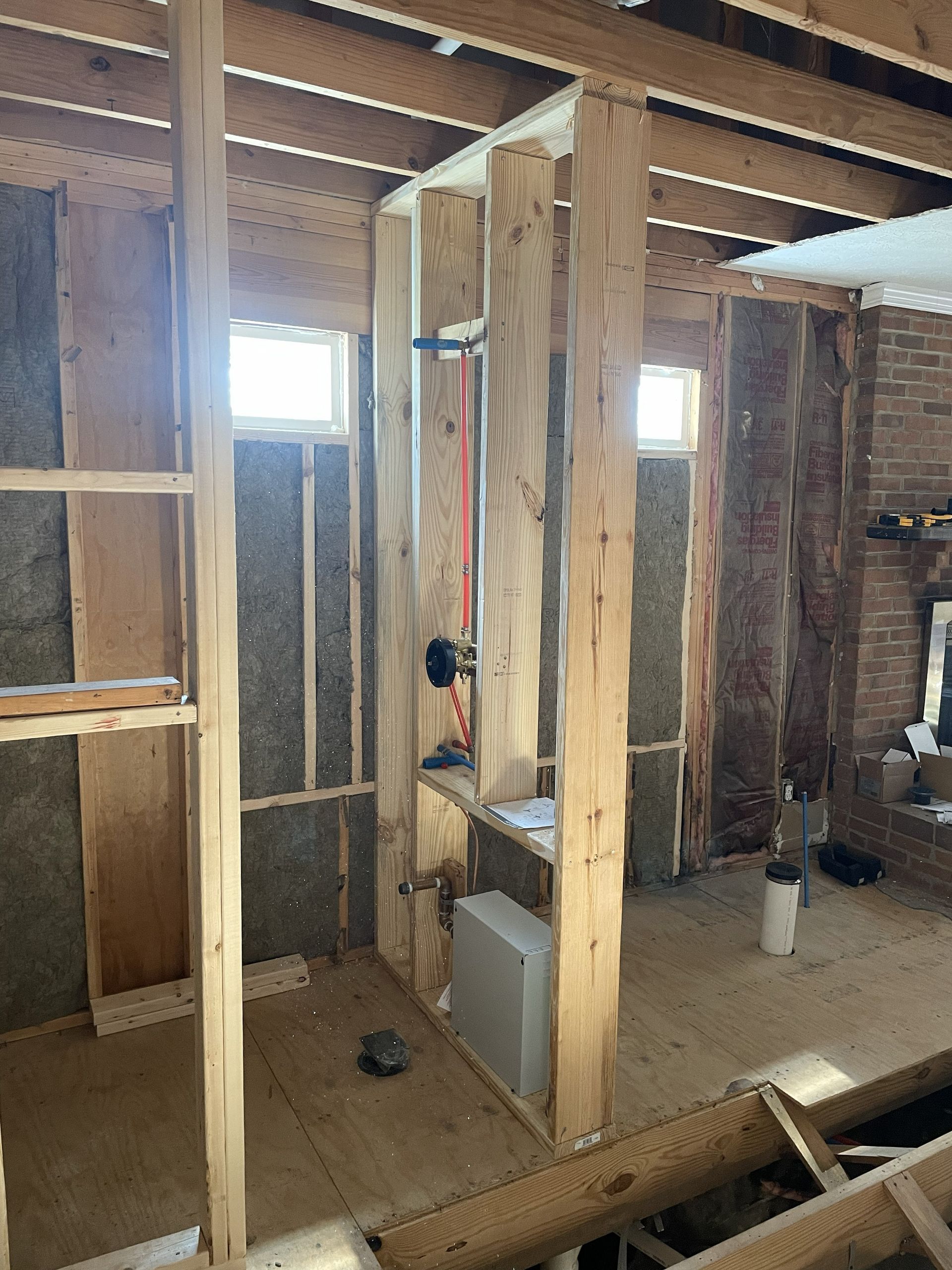Framed interior of a house under construction with exposed studs, plywood walls, and a small window.