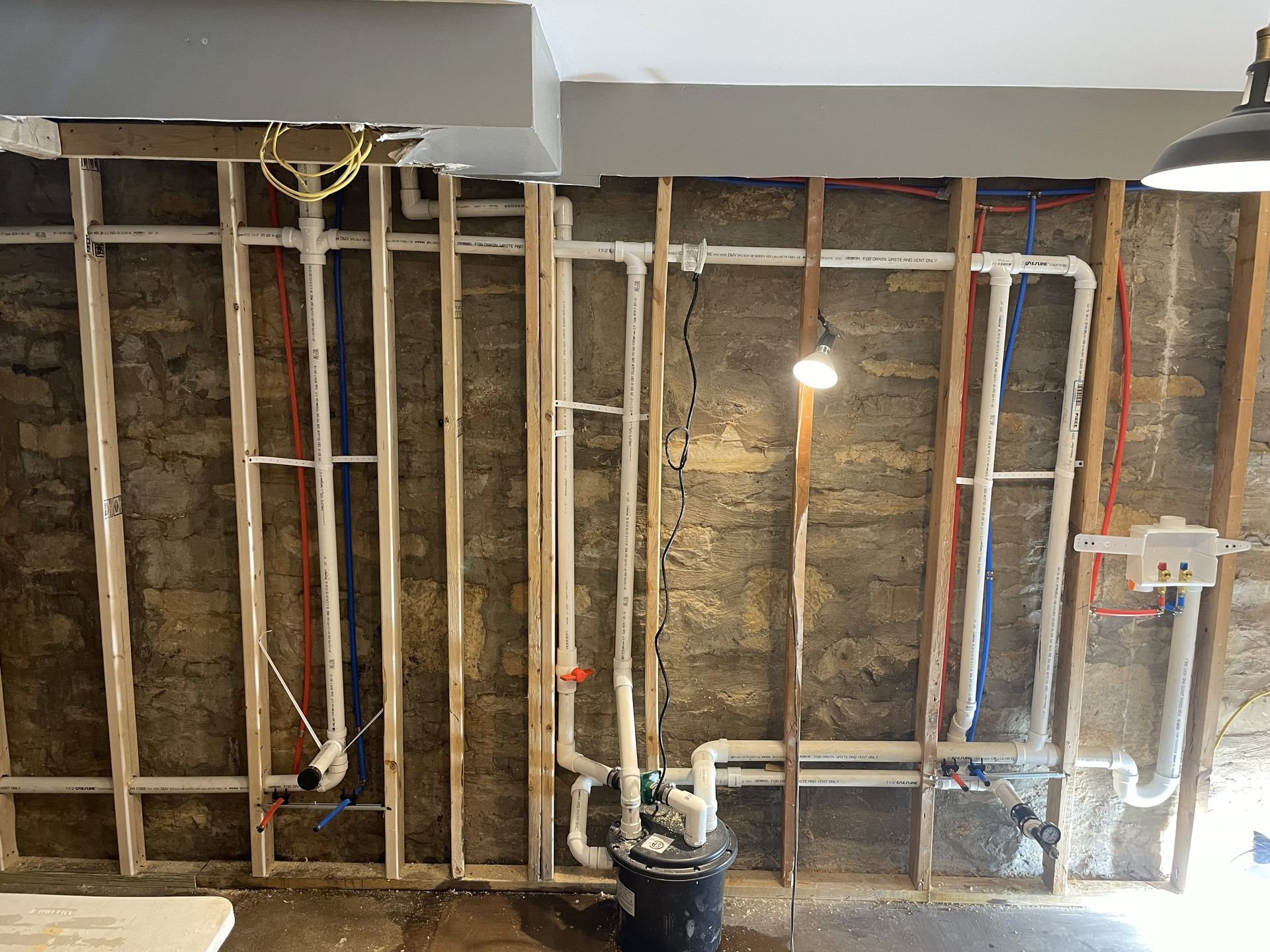 Partially renovated room with exposed wall studs, wiring, hanging light bulb, and construction bucket