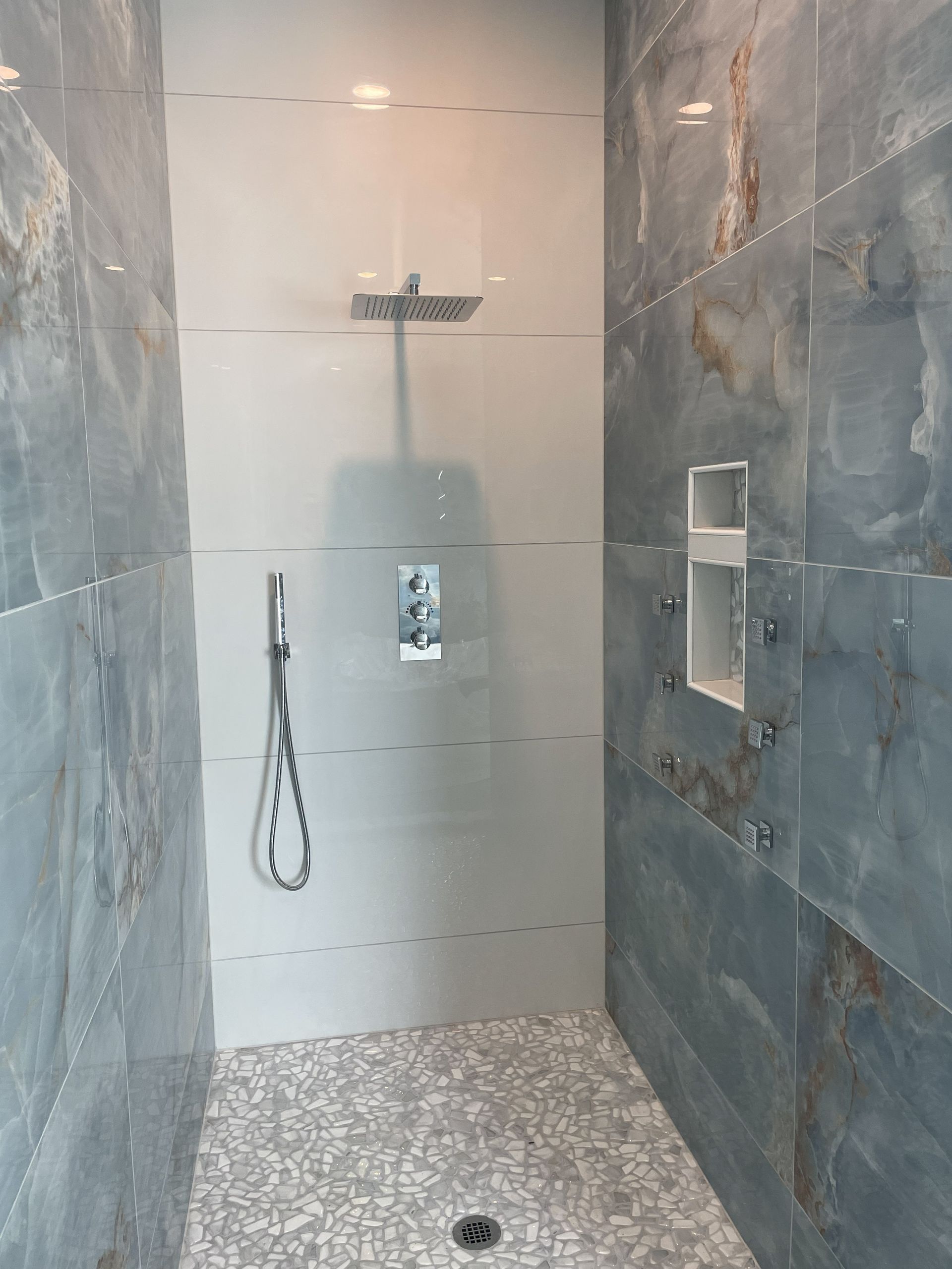 Modern tiled walk-in shower with rainfall head, handheld sprayer, and pebble shower floor.