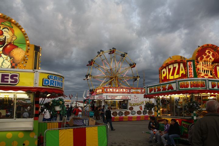 Fairground food stalls and a Ferris wheel under a cloudy sky at dusk