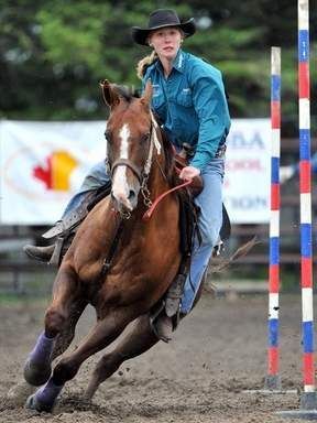 Cowboy in blue shirt and black hat racing a brown horse around a barrel course