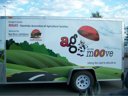 Branded trailer with green hills graphic and โagmooveโ text parked outdoors under a blue sky