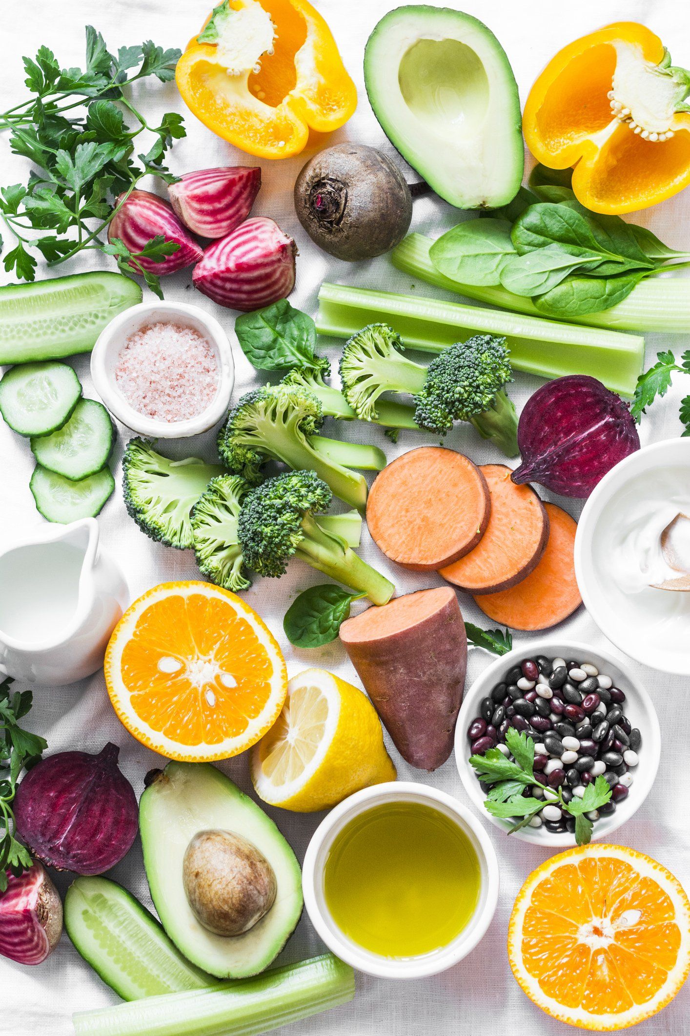 Assortimento di frutta e verdura fresca disposta su uno sfondo bianco, tra cui avocado, agrumi, barbabietole e broccoli.