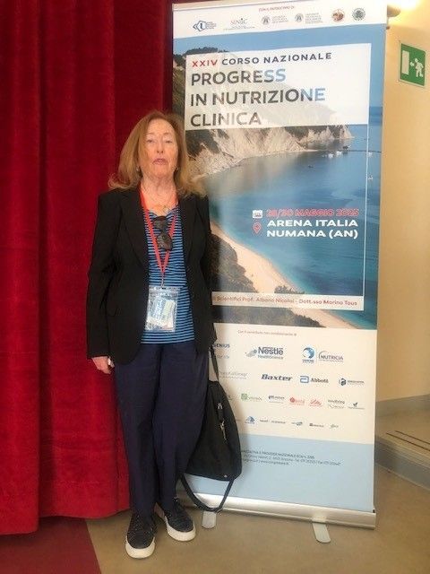Una donna in piedi accanto a uno striscione di una conferenza e a una tenda rossa
