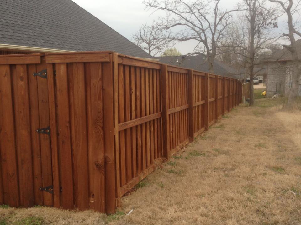 Long wooden privacy fence beside a beige yard, receding toward a gray house in a foggy backyard.