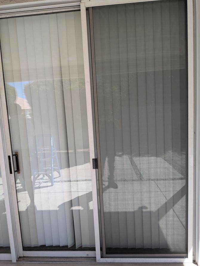 Sliding glass door with white vertical blinds and a screen. Bright outdoor setting.
