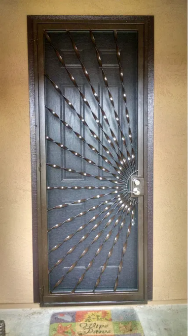 Metal security door with ornate spiral design. Bronze frame with screen, doormat at base.