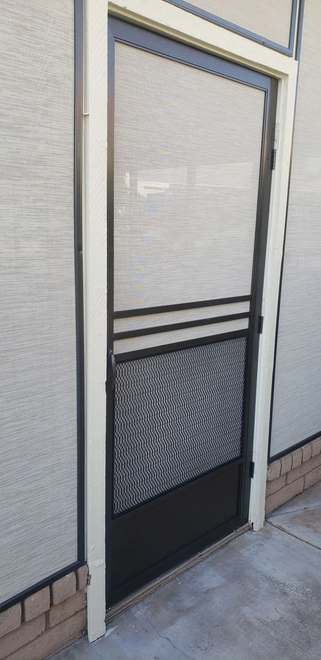 A black security door with a mesh screen, set in a white door frame, mounted on a brick and concrete exterior wall.