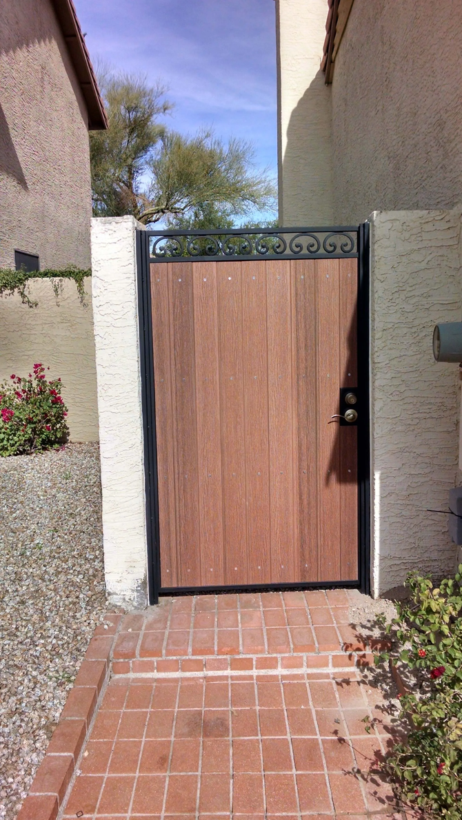 Wooden gate in brick walkway, flanked by textured walls, and foliage.