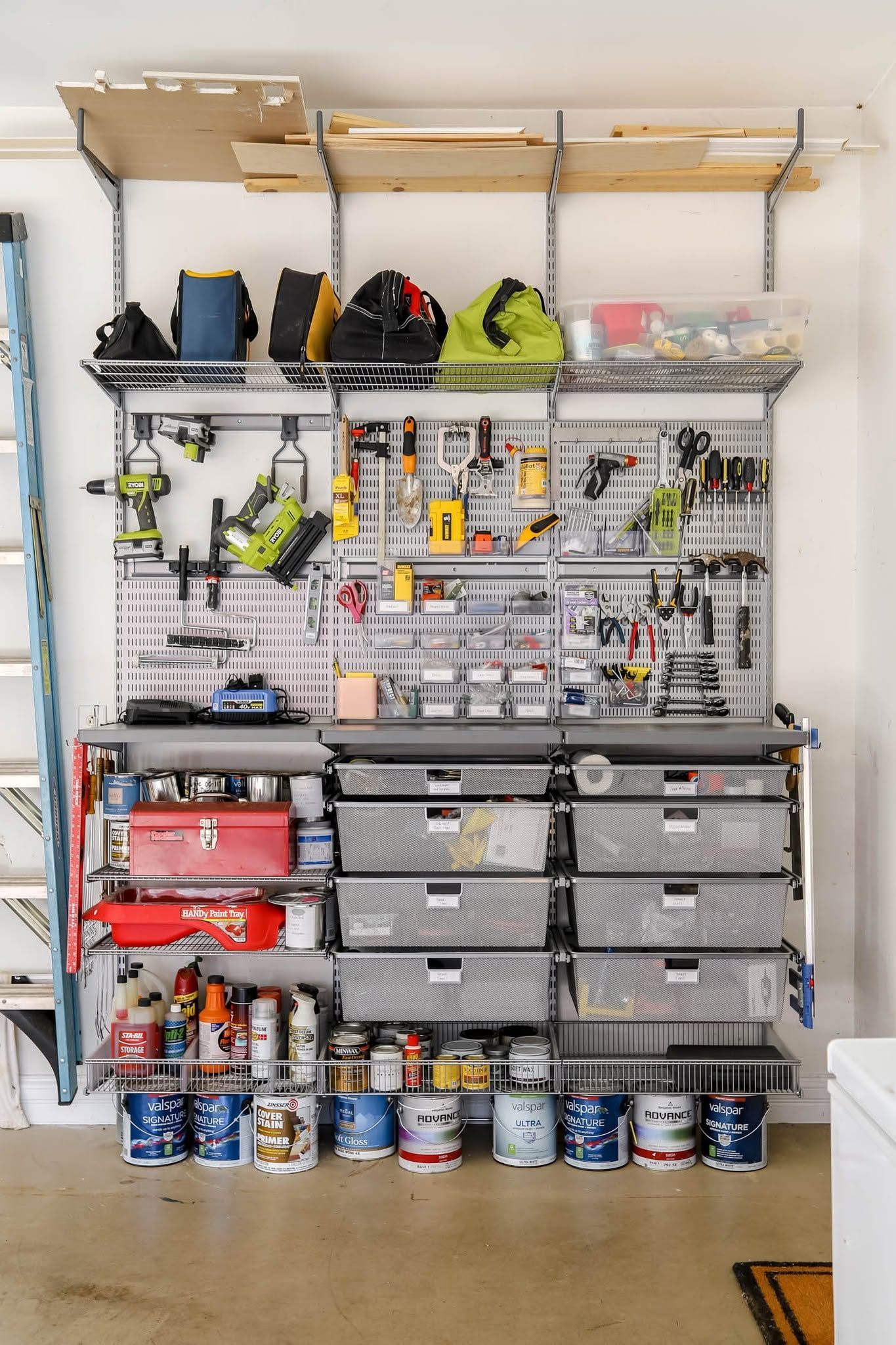 Garage wall with organized tool storage, shelves, bins, and cans on the floor