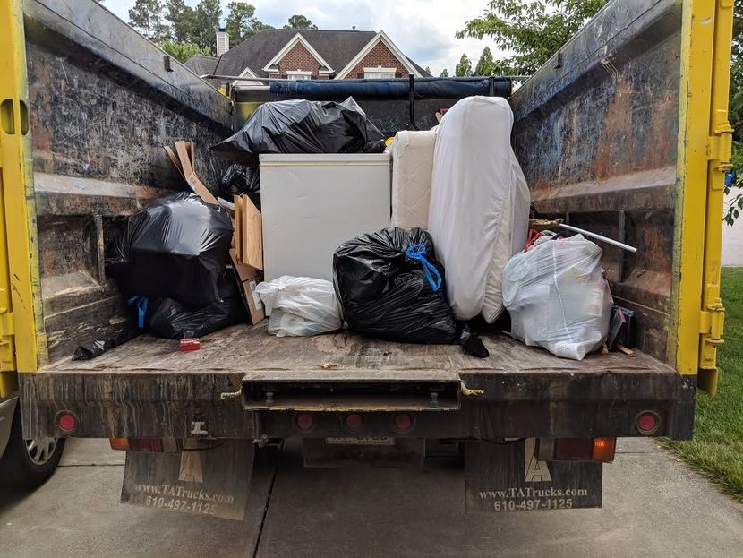 Truck bed loaded with black garbage bags, white sacks, and a mattress in a residential street