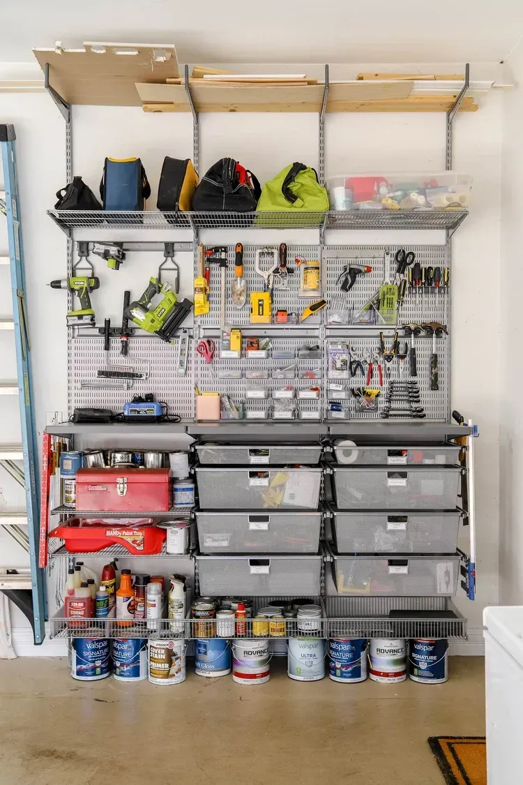 Garage wall with organized tool rack, shelves, storage bins, and spray cans on the floor