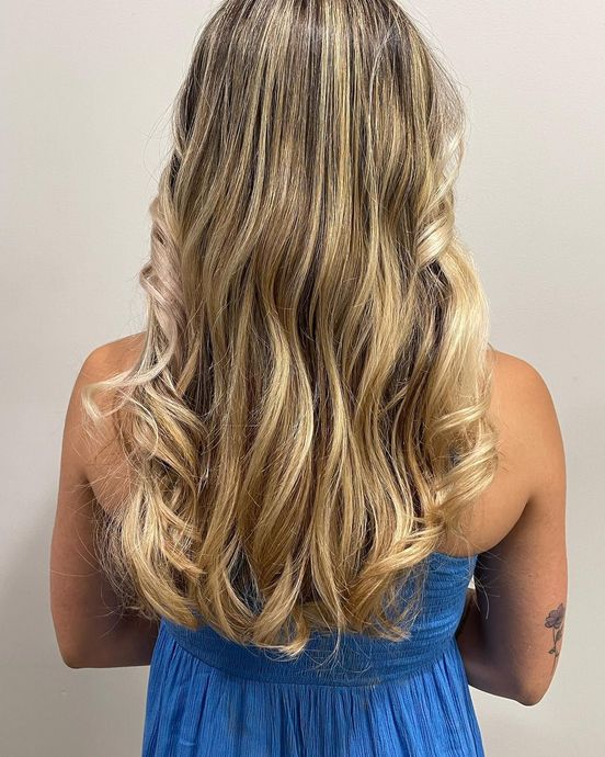 The back of a woman 's head with long blonde hair and a blue dress.