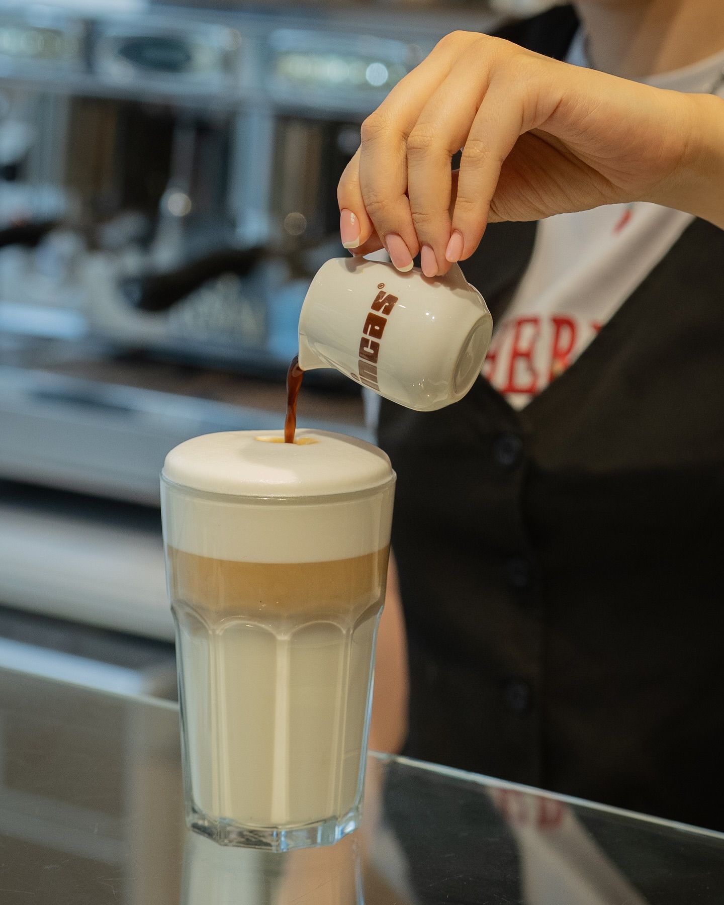 Barista pouring coffee into a layered latte in a clear glass.Domenica 
Home made italian pastries, food & coffee 
