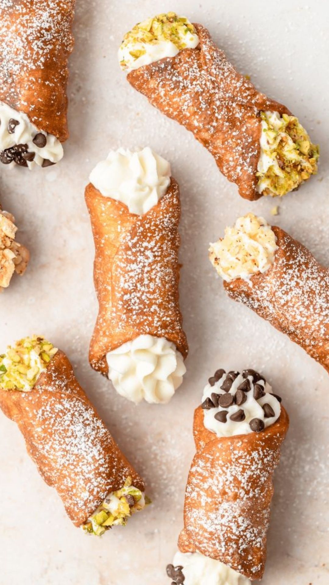 Close-up of assorted cream-filled pastries, some with coffee beans and powdered sugar, on a white surface.