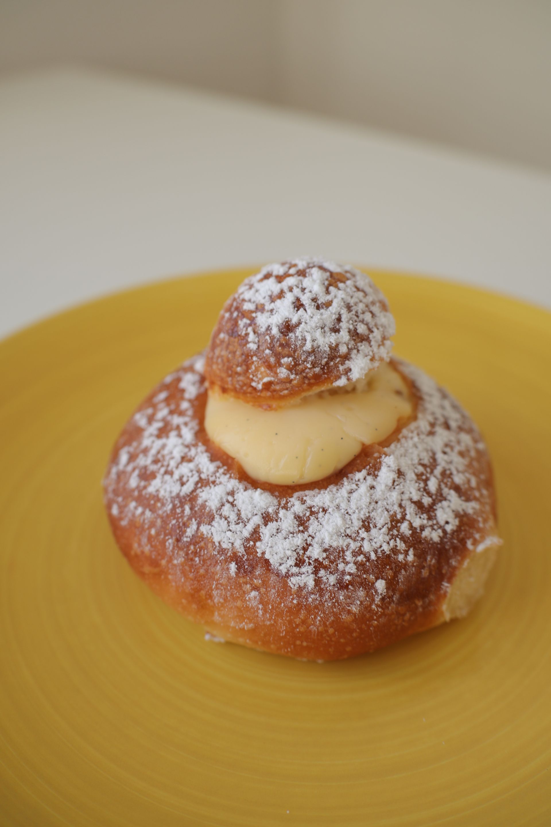 Brioche pastry topped with cream and powdered sugar on a yellow plate.