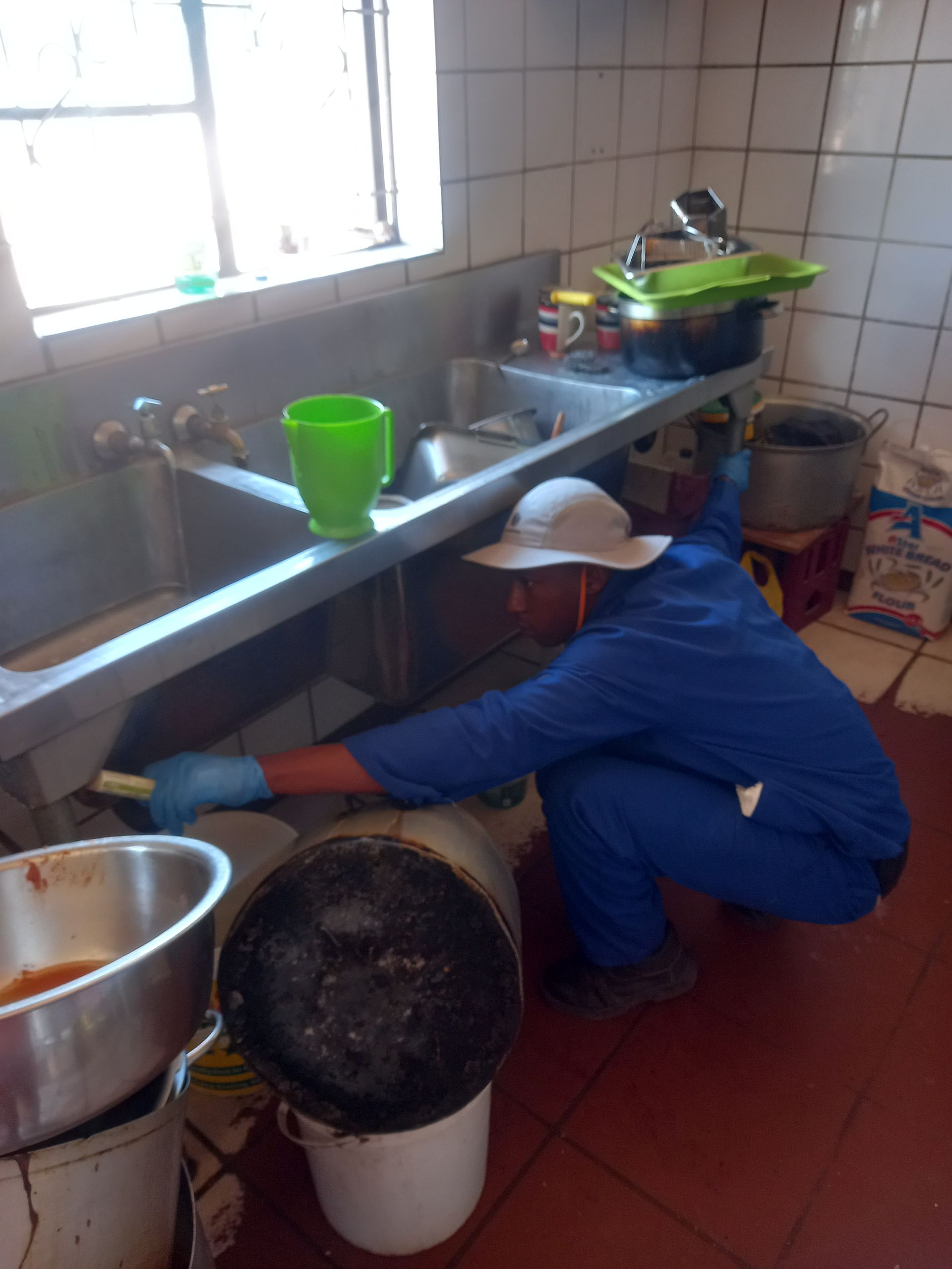 Person in blue coveralls cleans under a kitchen sink.