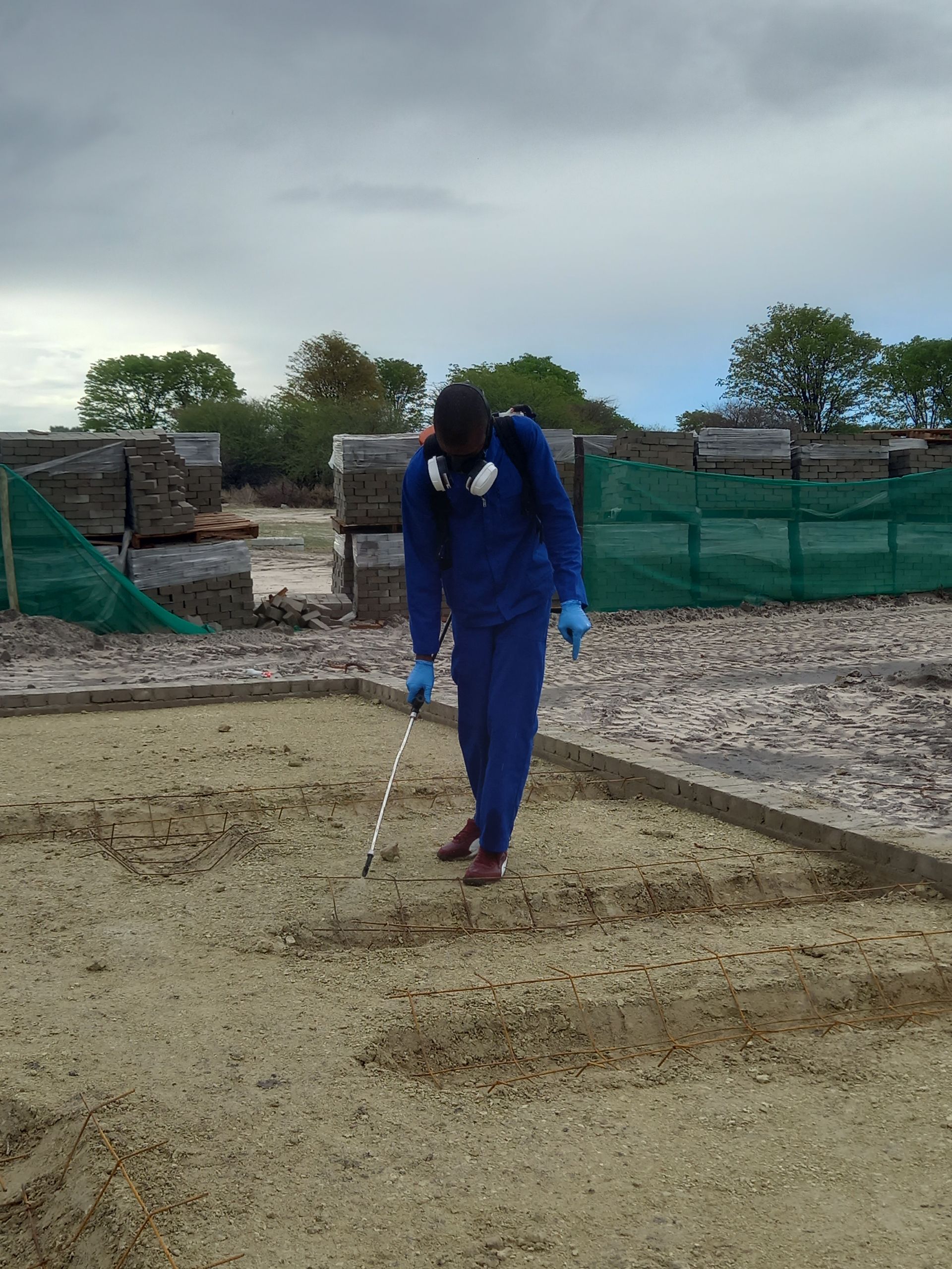 Person in blue protective suit inspecting a gravel bed with a measuring stick outdoors.