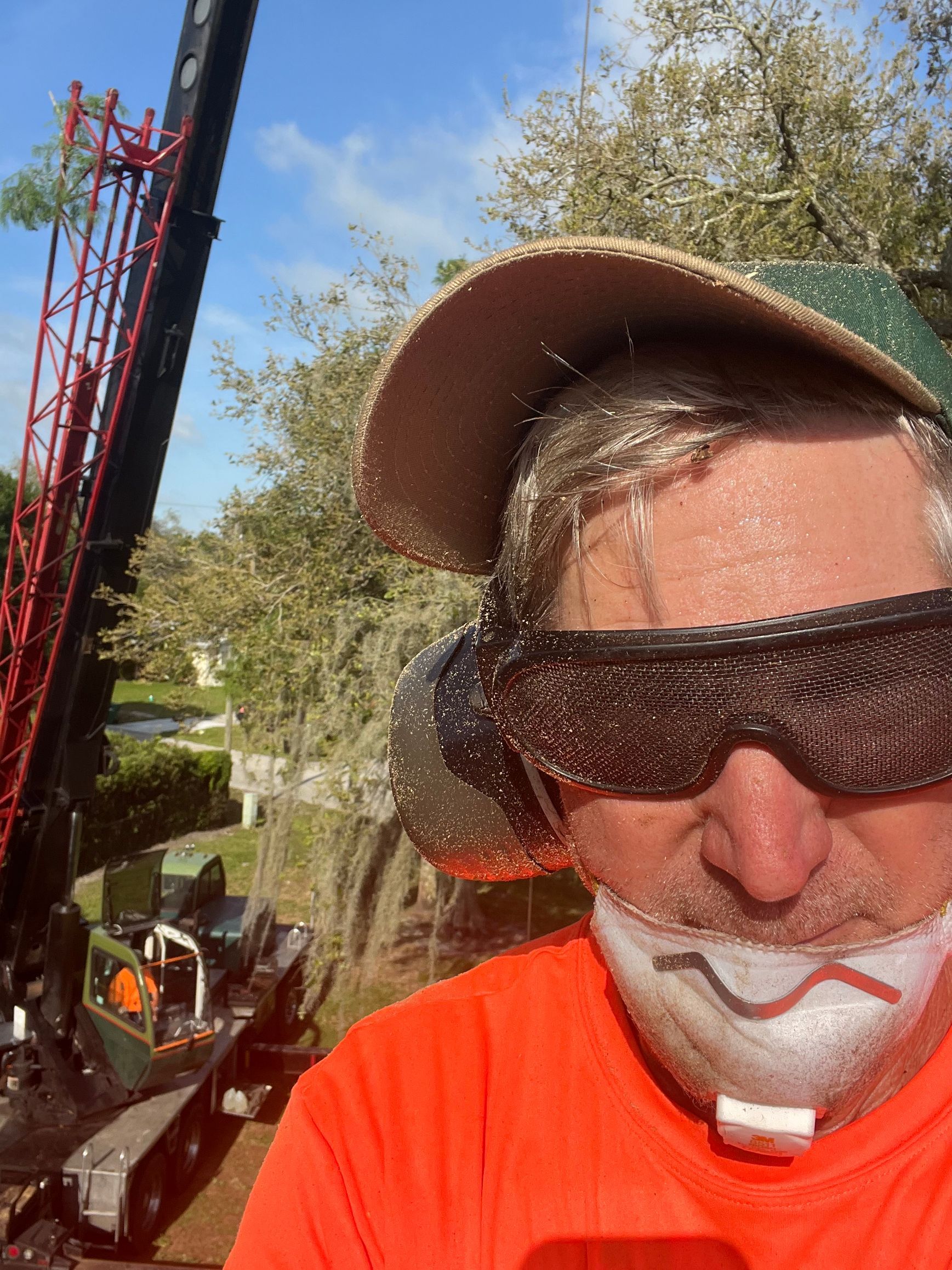 Man in orange shirt and cap wearing sunglasses, outdoors beside fishing rods under a blue sky