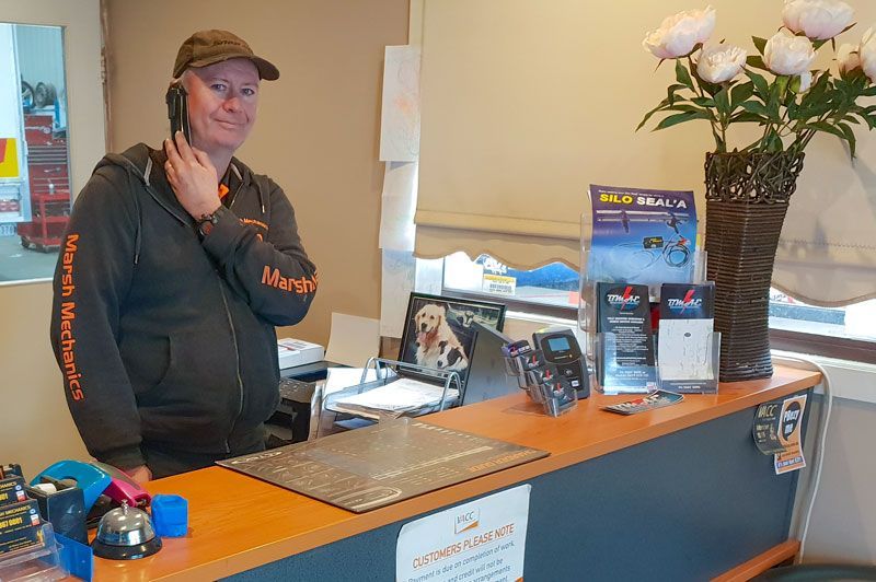 A Man Is Standing at A Counter Talking on A Cell Phone — Marsh Mechanics and Auto Electrical in Maddingley, VIC