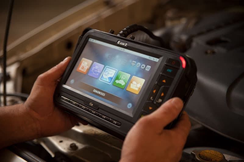 A Person Is Holding a Tablet in Their Hands in Front of A Car Engine For The Diagnostics — Marsh Mechanics and Auto Electrical in Maddingley, VIC