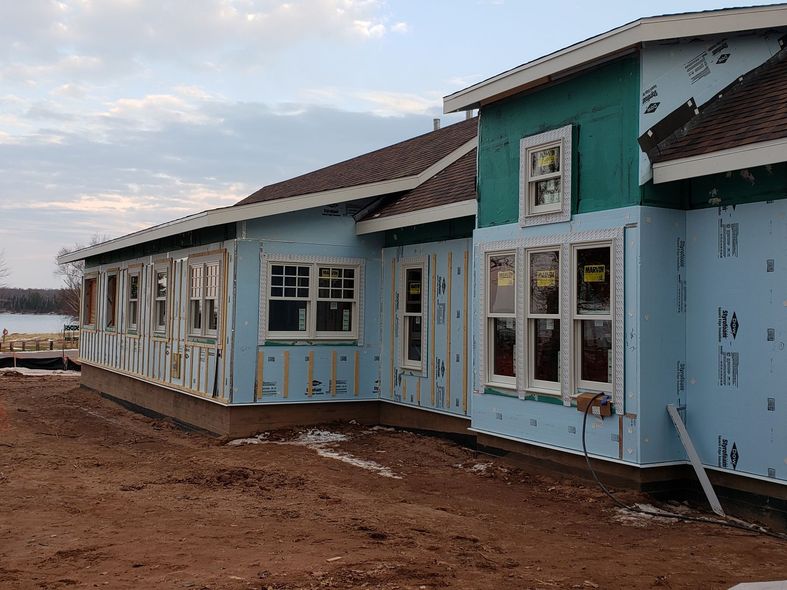 Row of light blue houses with white trim on a red dirt lot under a cloudy sky