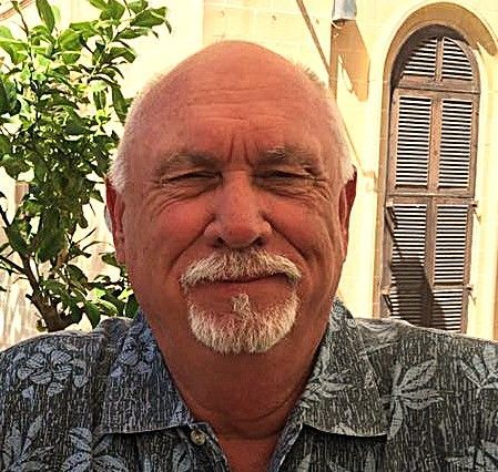 Smiling bald man with a white goatee in a patterned shirt
